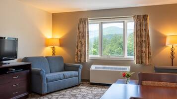 A hotel room with a sofa, a TV, a table, and a window with curtains.
