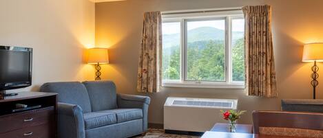 A hotel room with a sofa, a TV, a table, and a window with curtains.