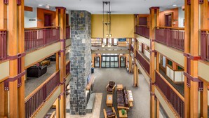 A multi-level hotel lobby with a central stone column, wooden railings, and a seating area with tables and chairs. - Grand Summit Hotel at Attitash (Bartlett)