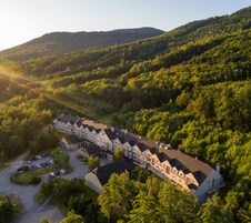 A large, multi-story hotel with a symmetrical facade, surrounded by dense forest and hills.