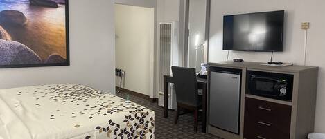 Una habitación de hotel con una cama, un escritorio con computadora, televisión y microondas.
