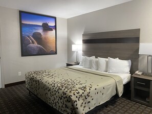 Ett hotellrum med en säng, ett nattduksbord, en lampa och en tavla som föreställer ett kustlandskap.