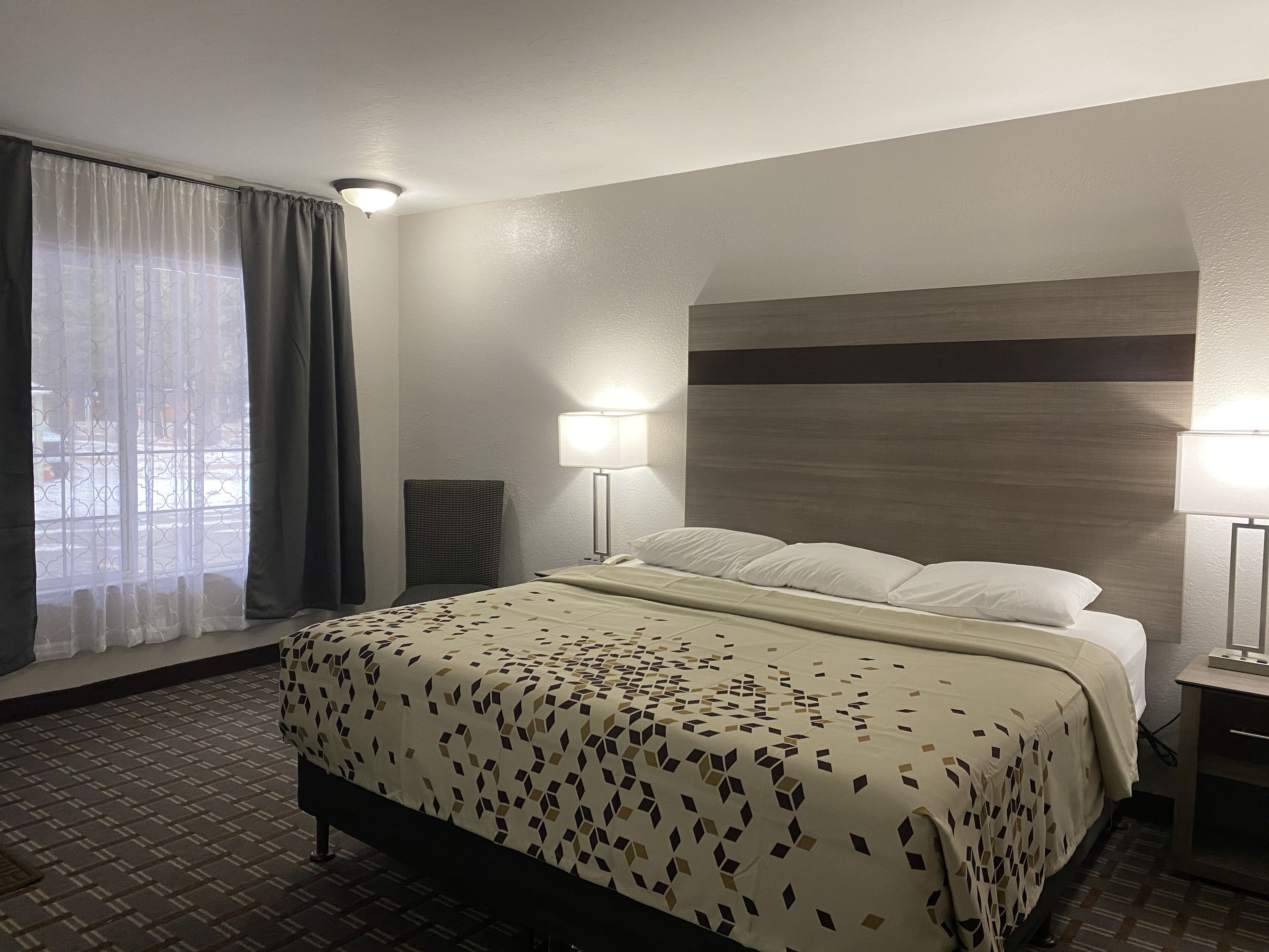 Una habitación de hotel con cama, dos lámparas de noche, una ventana con cortinas y cabecero.
