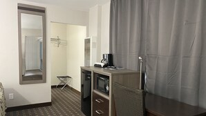Une chambre d’hôtel compacte comprenant une kitchenette, un petit coin salon et un miroir.