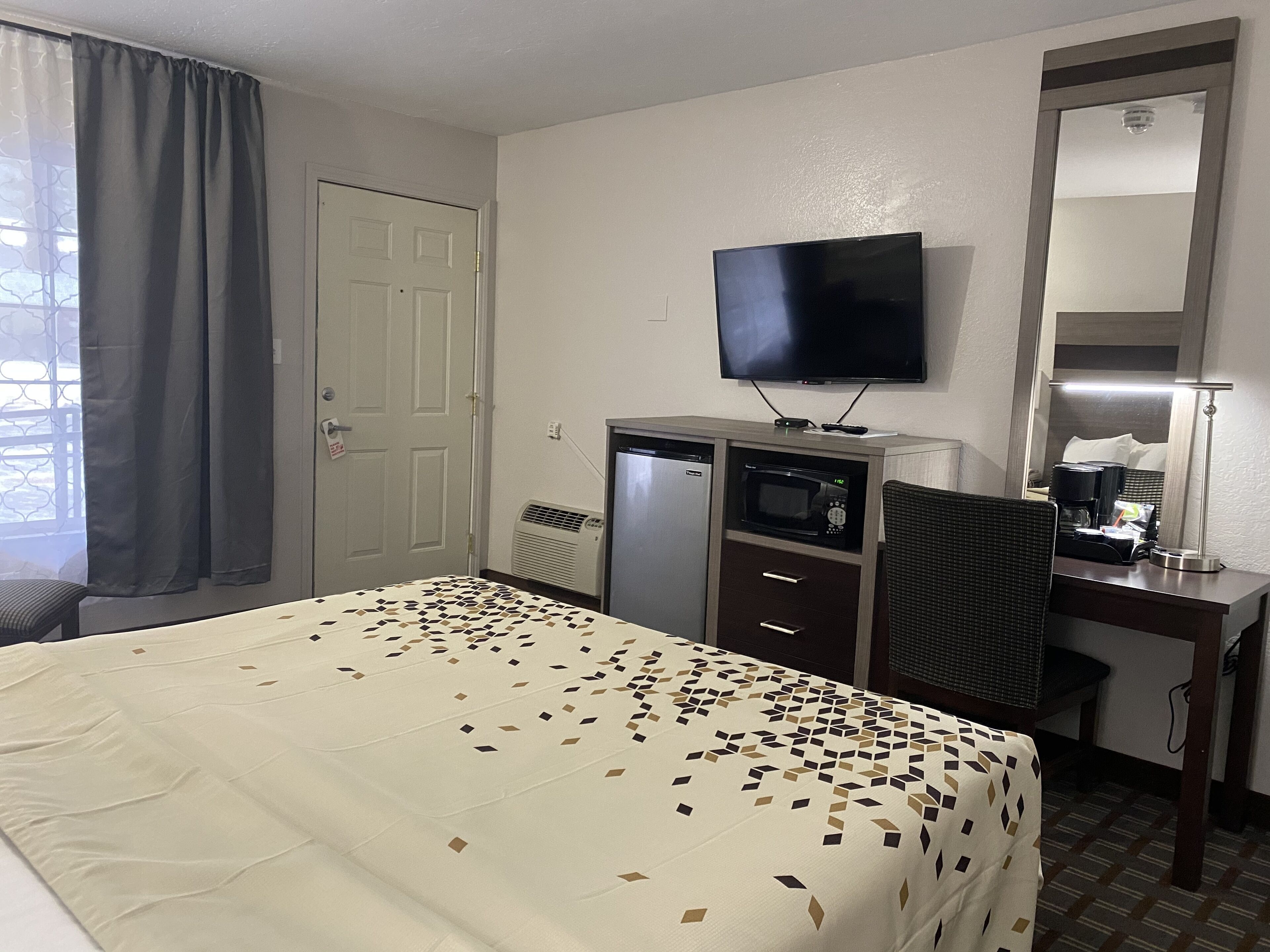 A hotel room with a bed, a desk with a computer, a television, and a mirror.