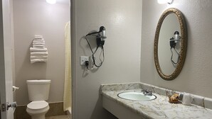 A bathroom with a toilet, a sink with a marble countertop, a wall-mounted mirror with an ornate frame, and a hairdryer on the wall. - High Country Lodge (South Lake Tahoe)