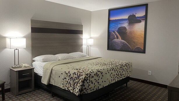 A hotel room with a bed, bedside lamps, a telephone, a small table, and a framed picture on the wall. - High Country Lodge (South Lake Tahoe)