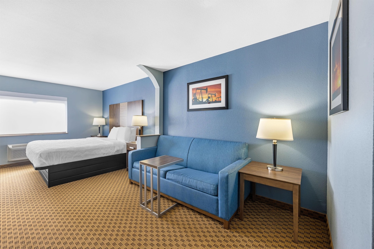 A hotel room with a bed, a blue sofa, a small table, a lamp, and a painting on the wall.