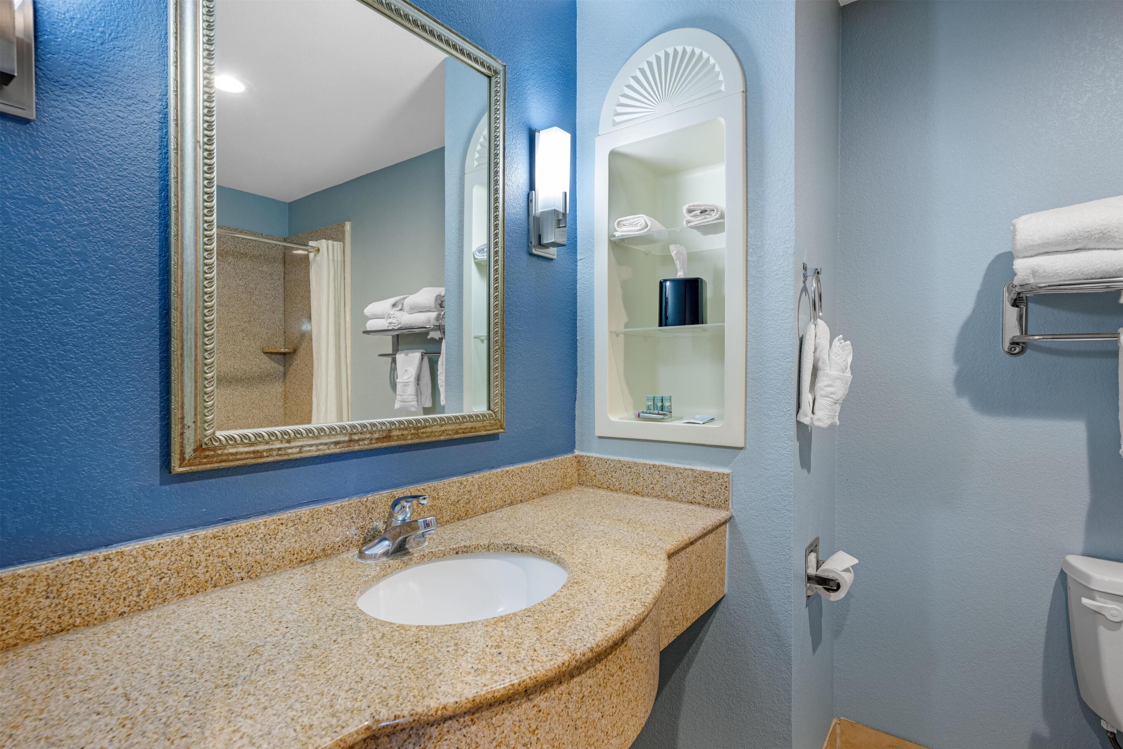 A bathroom with a granite countertop sink, a large mirror, a towel rack, and a toilet.