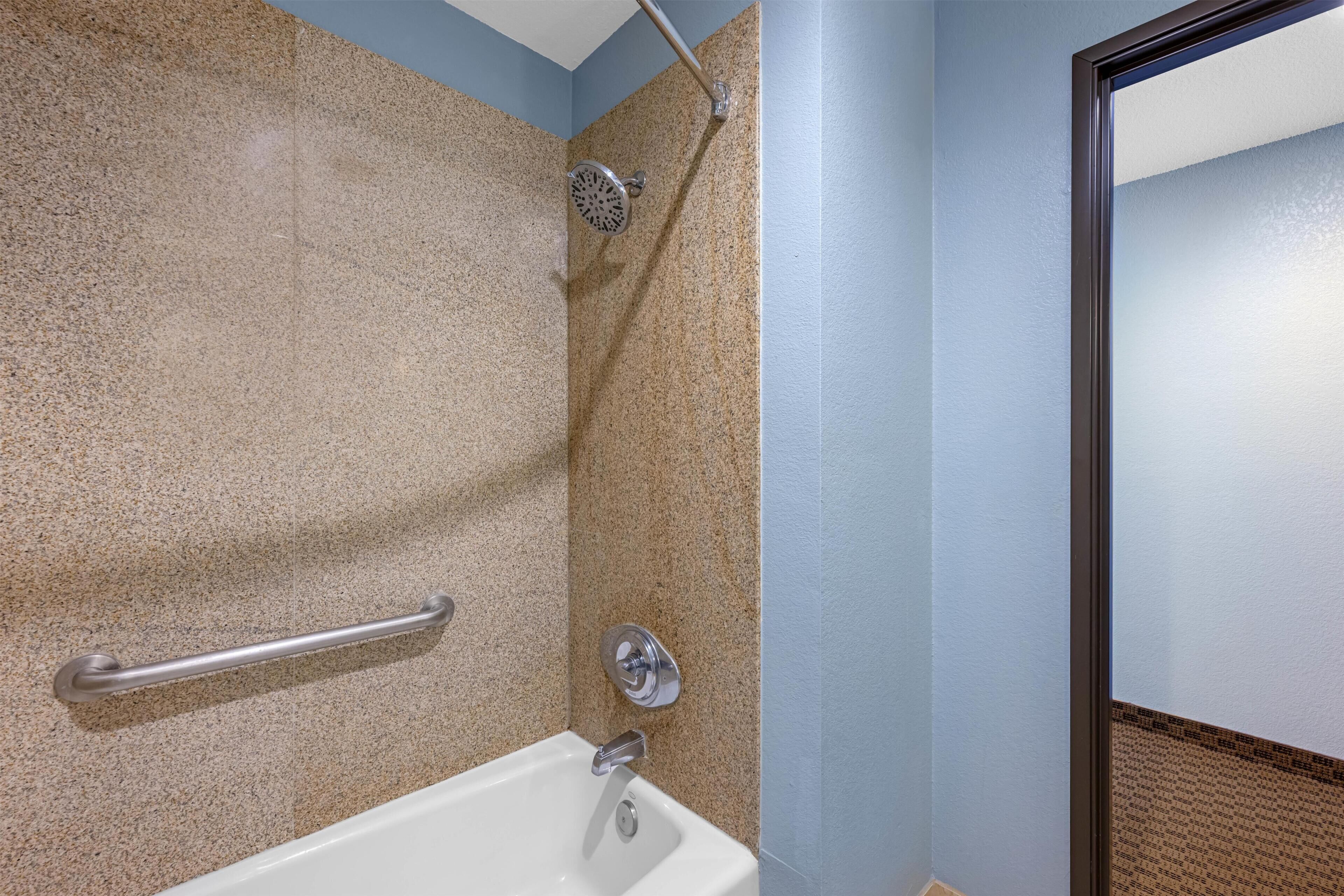 A bathroom with a bathtub, a shower, and a handrail.