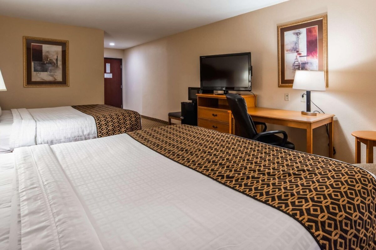 Quarto de hotel com duas camas, uma mesa de escritório com computador e televisão, e uma pequena mesa.