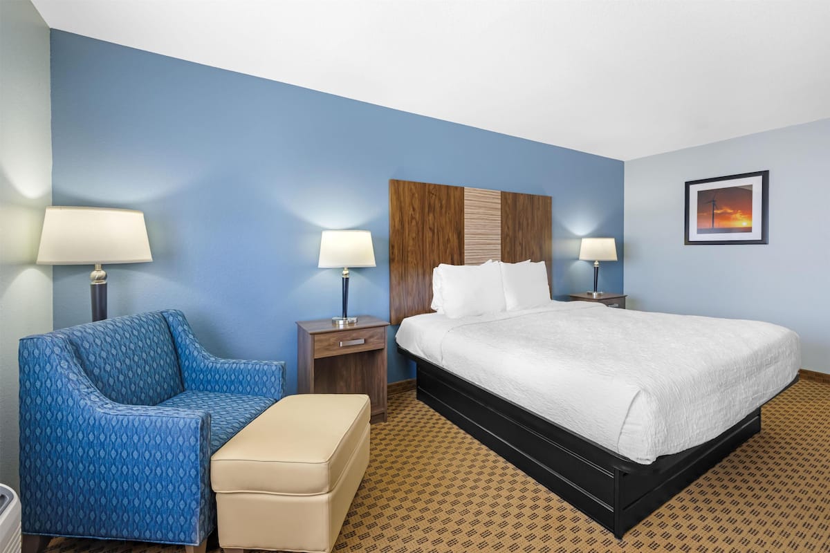 A hotel room with a bed, a sofa, a nightstand, a lamp, and a picture on the wall.