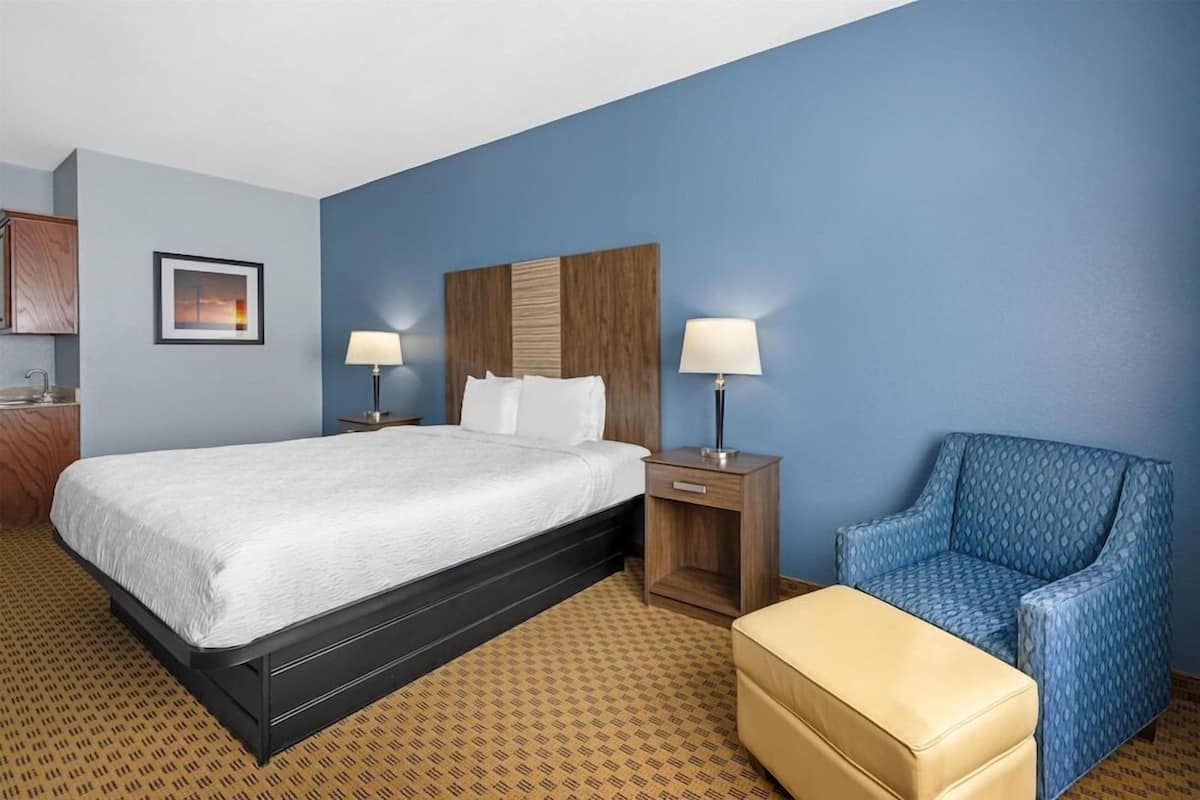 A hotel room with a bed, bedside tables, a chair, and a small table.