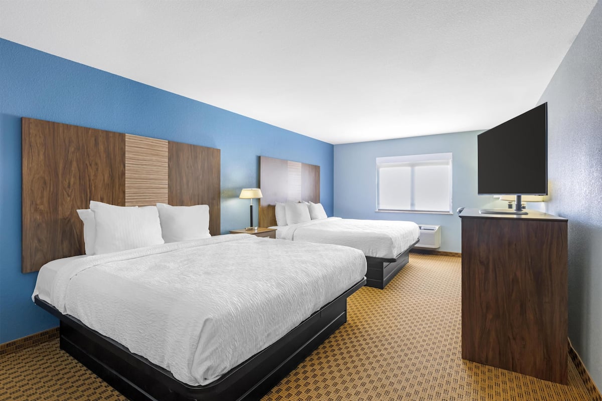 A hotel room with two beds, a desk, a TV, and a window.