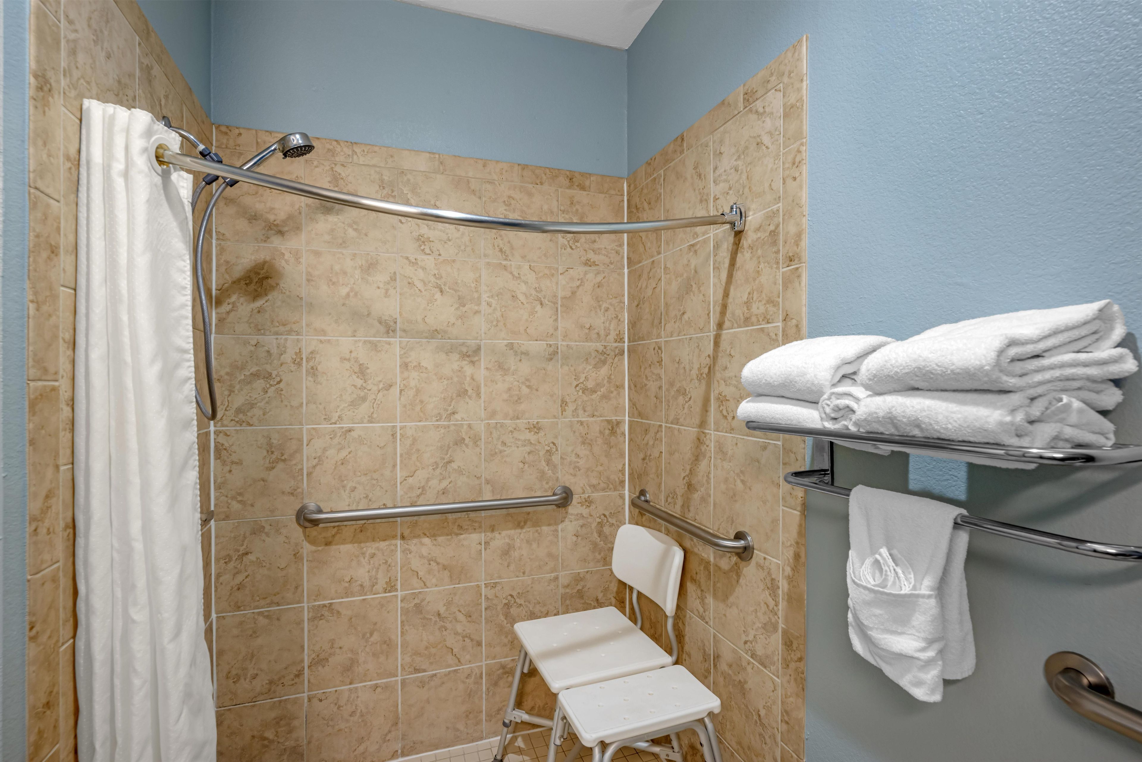 Une salle de bain équipée d’une douche, de barres d’appui, d’une chaise blanche et d’un porte-serviettes.