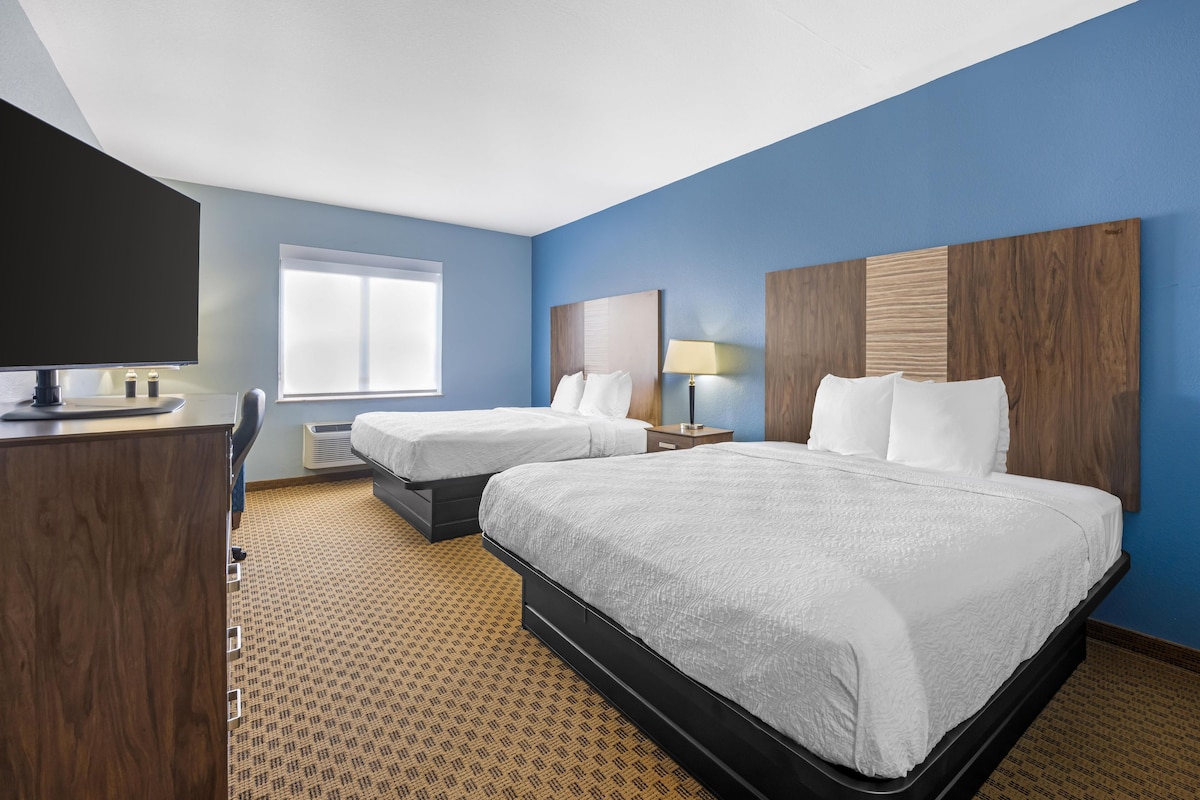 A hotel room with two beds, a desk, a TV, and a window.