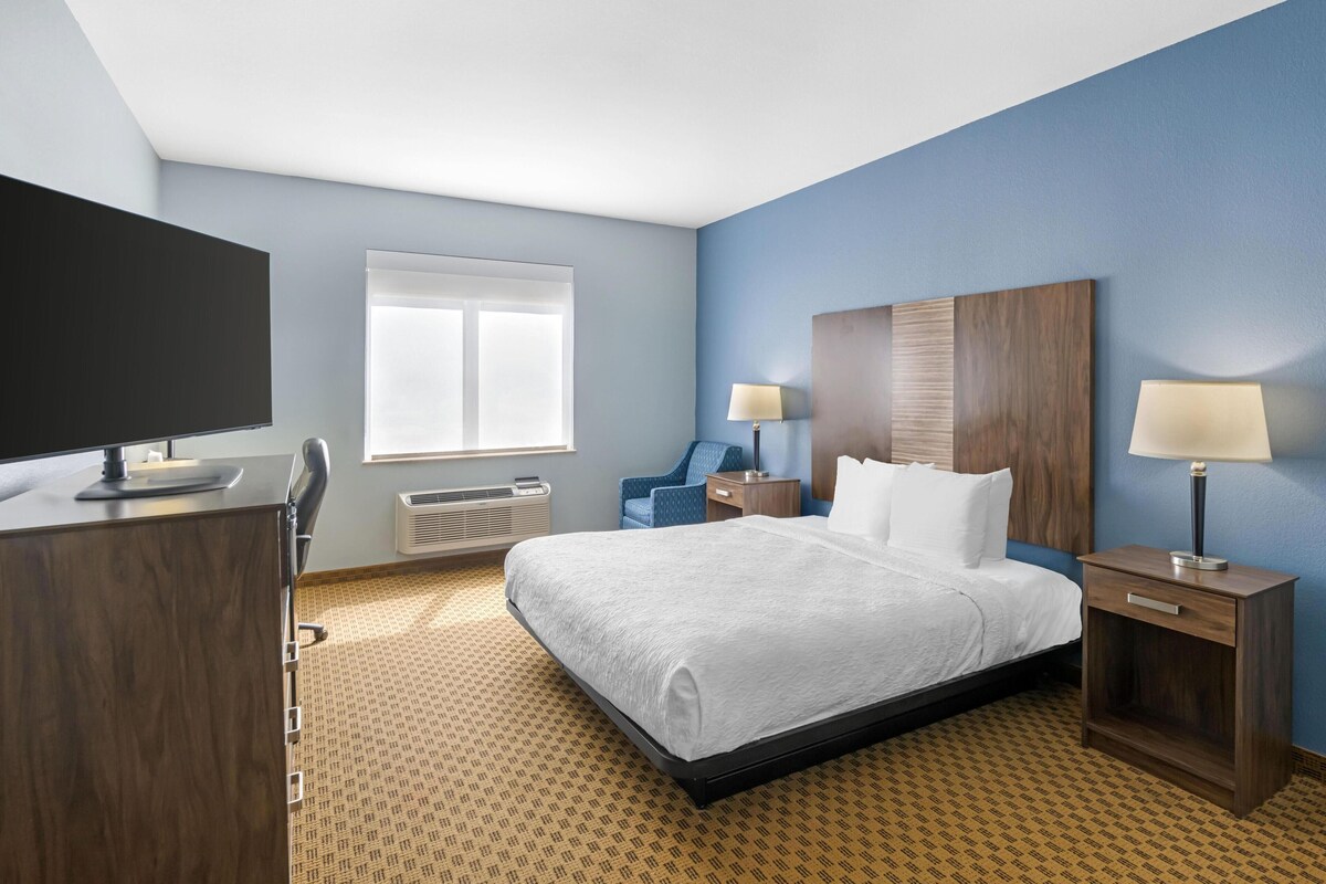 Een hotelkamer met een bed, nachtkastjes, een bureau, een stoel, een televisie en een raam.