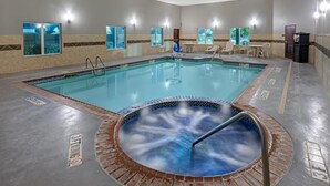Una piscina con jacuzzi, paredes de azulejos y una zona de estar con sillas y mesas.