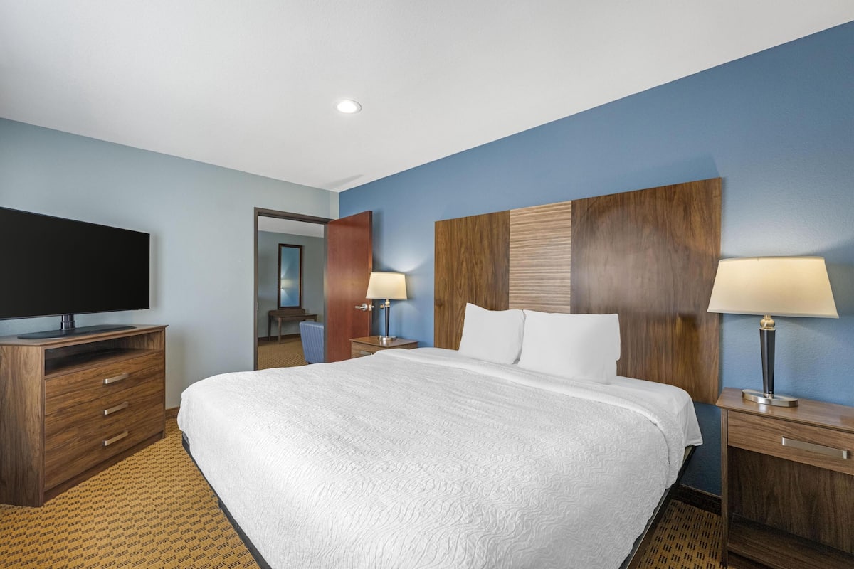 A hotel room with a large bed, a flat-screen TV, wooden nightstands, and a mirror.