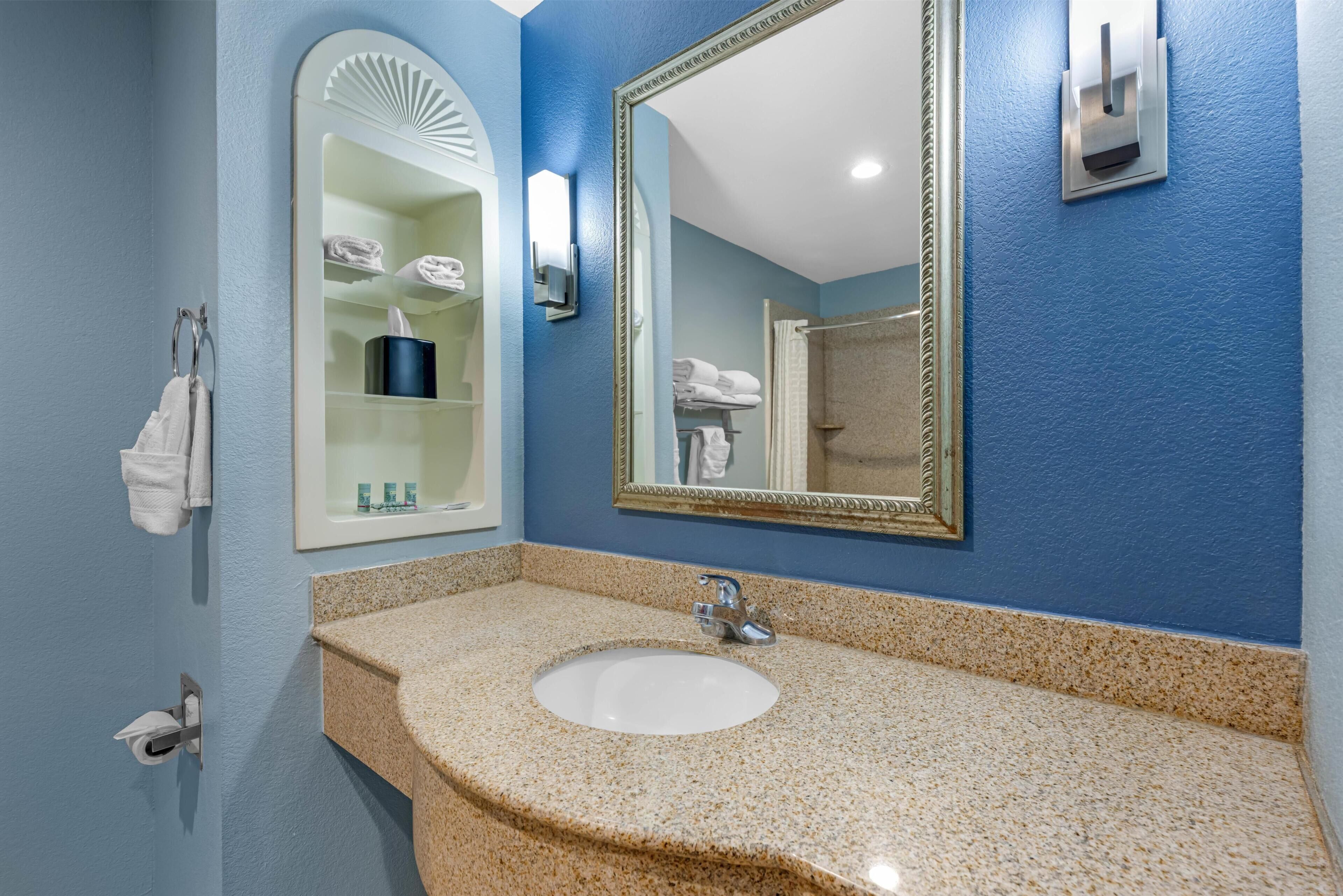 Un bagno con un lavandino, due specchi, un portasciugamani e uno scaffale con articoli da toilette.