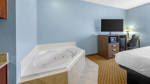 Habitación de hotel con bañera, escritorio con silla, televisión y cama.