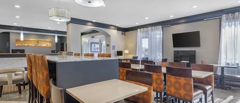 A hotel dining area with tables and booths, a counter, and a TV screen.