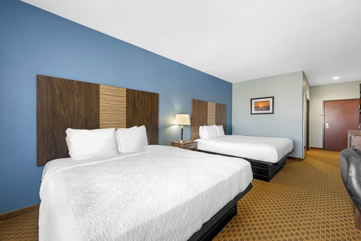 A hotel room with two beds, a nightstand with a lamp, a framed picture on the wall, and a door.