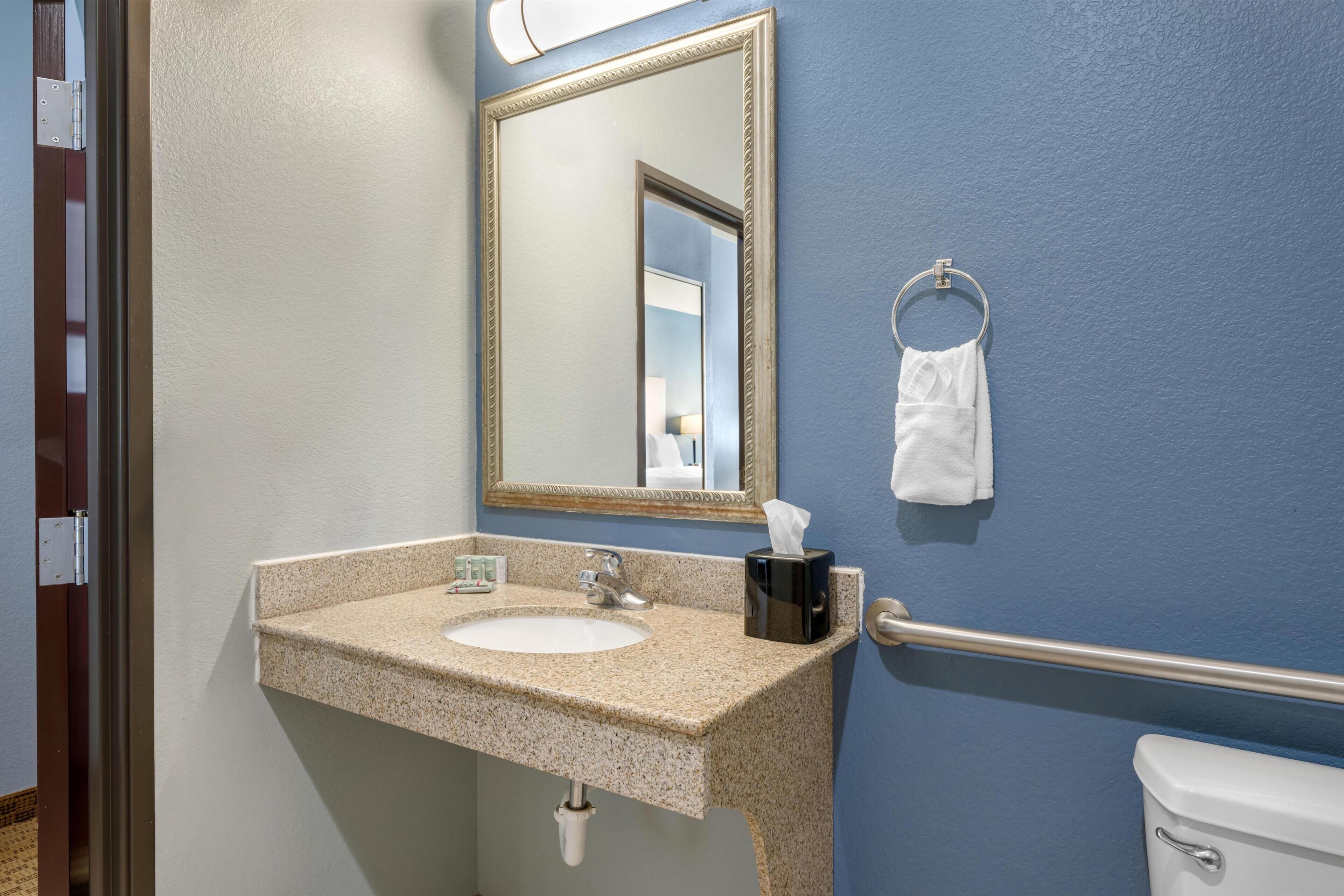 A bathroom with a sink, mirror, towel ring, and toilet.