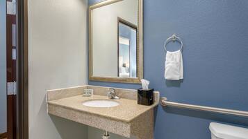 A bathroom with a sink, mirror, towel ring, and toilet.