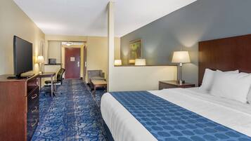 A hotel room with a large bed, a desk with a computer, a chair, a TV, and a desk lamp.