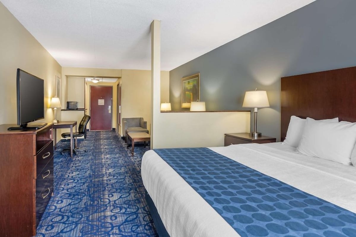 A hotel room with a bed, desk, chair, TV, and a door leading to another room.