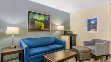 A hotel room with a blue sofa, a grey armchair, a wooden coffee table, two lamps, a microwave, and a small cabinet.