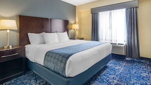 Ein Hotelzimmer mit einem großen Bett, zwei Nachttischen mit Lampen, einem Fenster mit Vorhängen und einem Teppich mit blauem Muster.