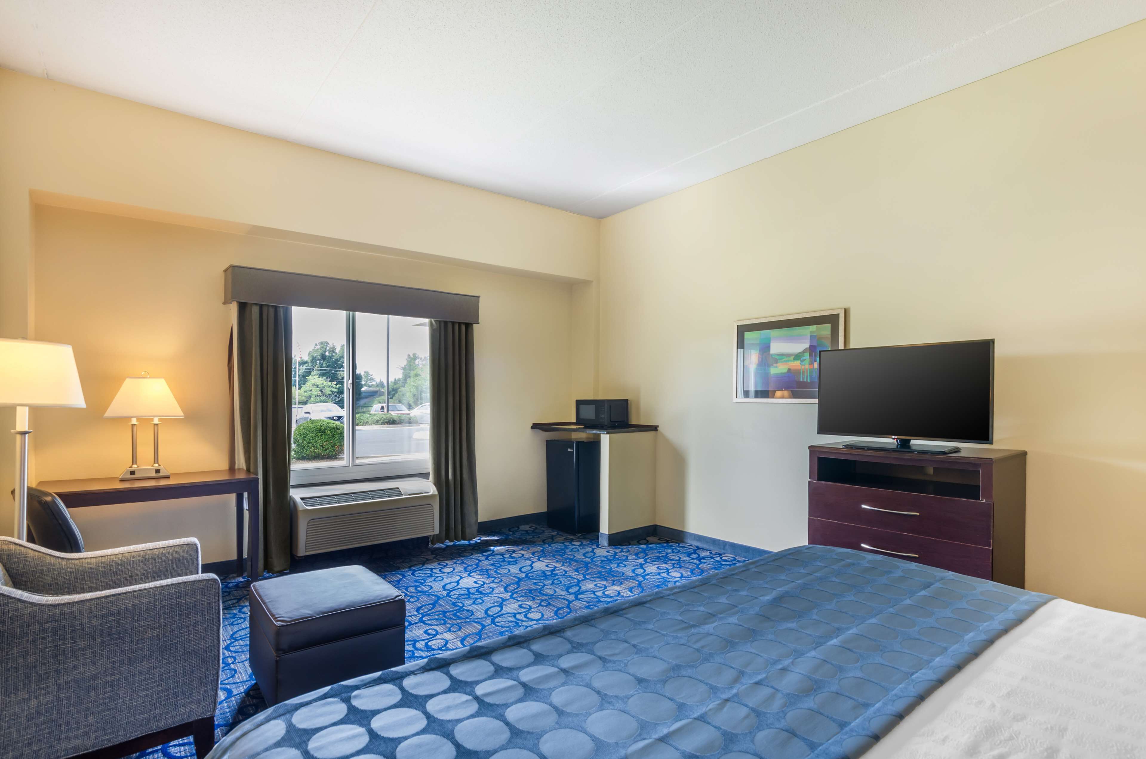A hotel room with a bed, a desk, a chair, a television, and a window with curtains.