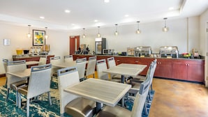 Ein Hotelrestaurant mit Tischen, Stühlen, einer Küchenzeile und Pendelleuchten.