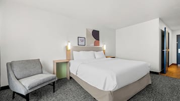 Una habitación de hotel con cama, silla, mesita de noche y lámpara de pared.