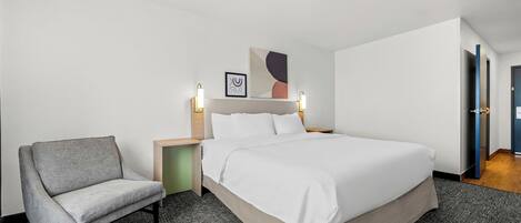 Une chambre d’hôtel avec un lit, une chaise, une table de chevet et une lampe fixée au mur.