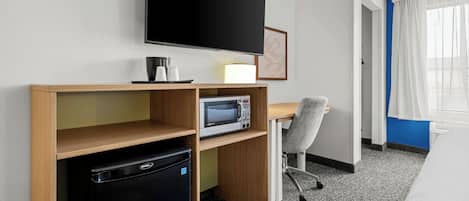 Habitación de hotel con televisión de pantalla plana, microondas, mini refrigerador, escritorio, silla y cama.