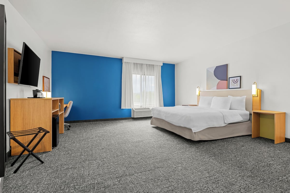A hotel room with a bed, desk, chair, TV, and artwork on the wall.