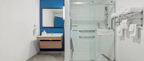 Un baño moderno con cabina de ducha de vidrio, tocador de madera, lavabo blanco y pared de acento azul.