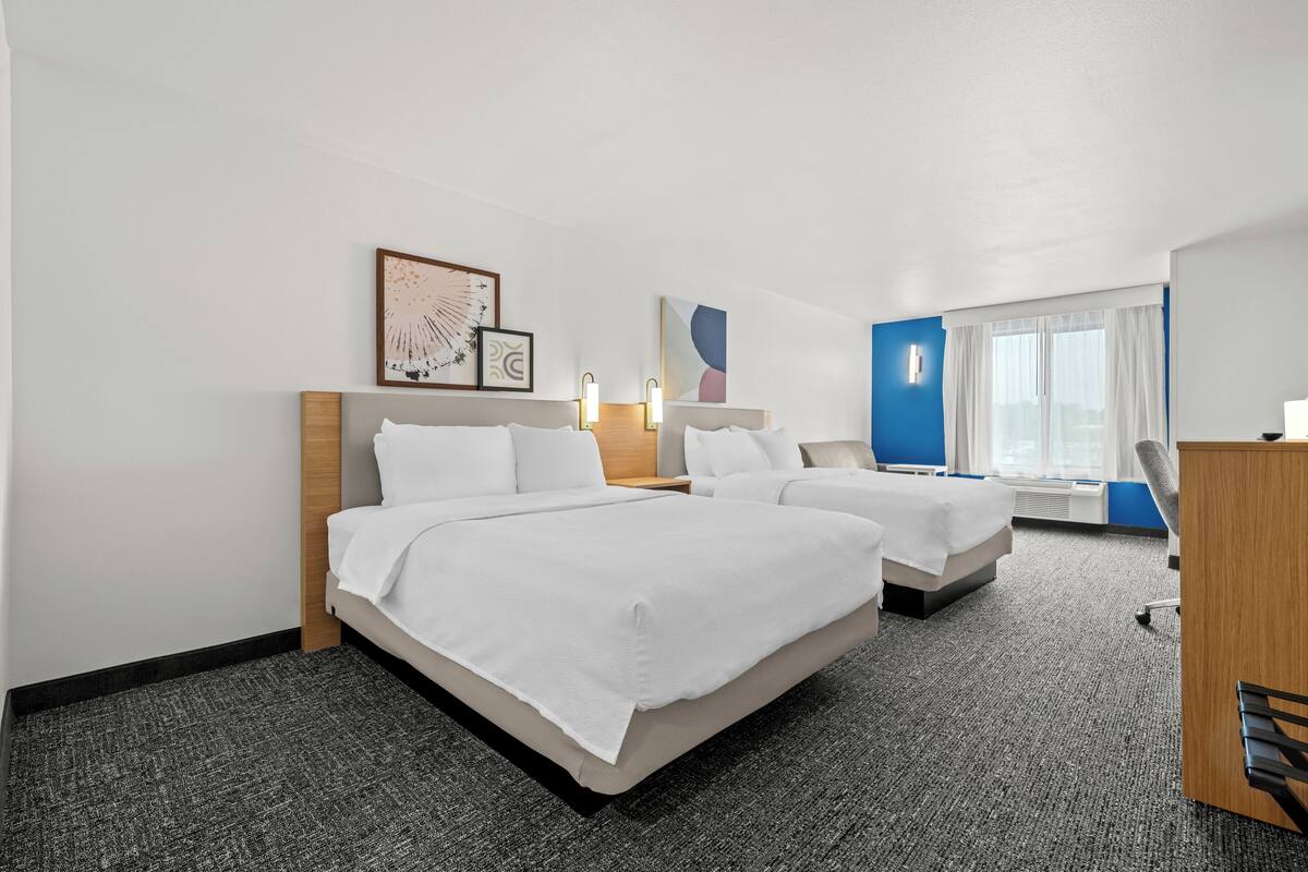 A hotel room with two beds, a desk, a chair, and artwork on the walls.