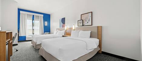 A hotel room with two beds, a desk, a chair, and a large window with curtains.