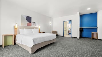 Habitación de hotel con cama, mesitas de noche, una silla, un escritorio y una pared azul decorativa.