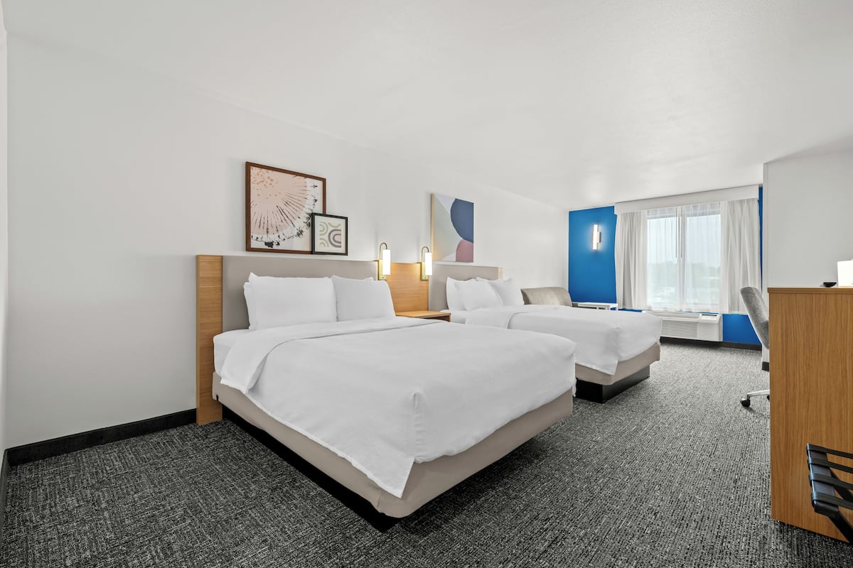 A hotel room with two beds, a desk, and a window with curtains.