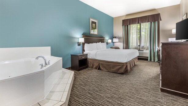 A hotel room with a large bed, a separate bathroom with a bathtub, a desk with a television, and a window with curtains. - Best Western Mineola Inn (Mineola)
