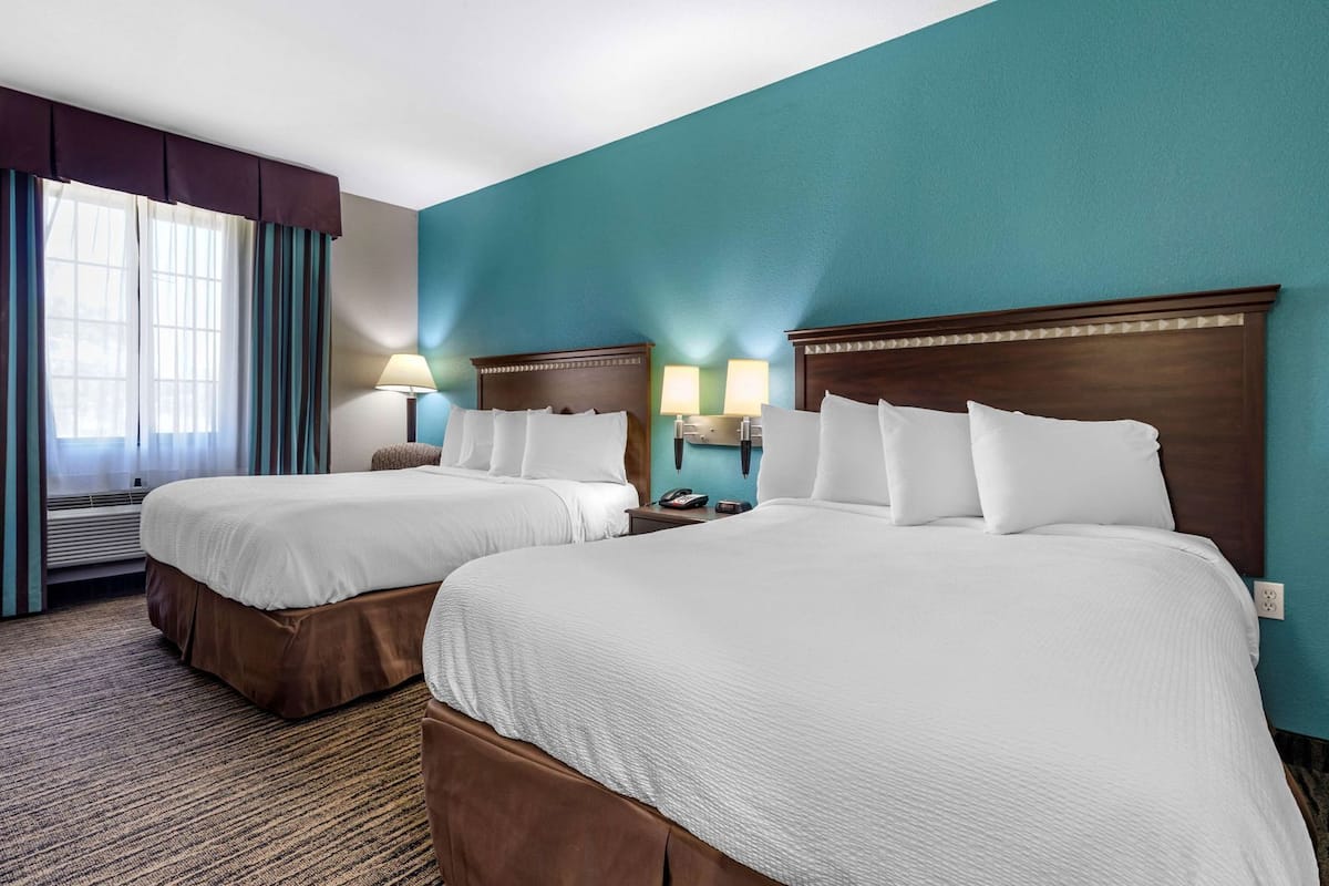 A hotel room with two beds, a window with curtains, a wall-mounted lamp, and a carpeted floor.