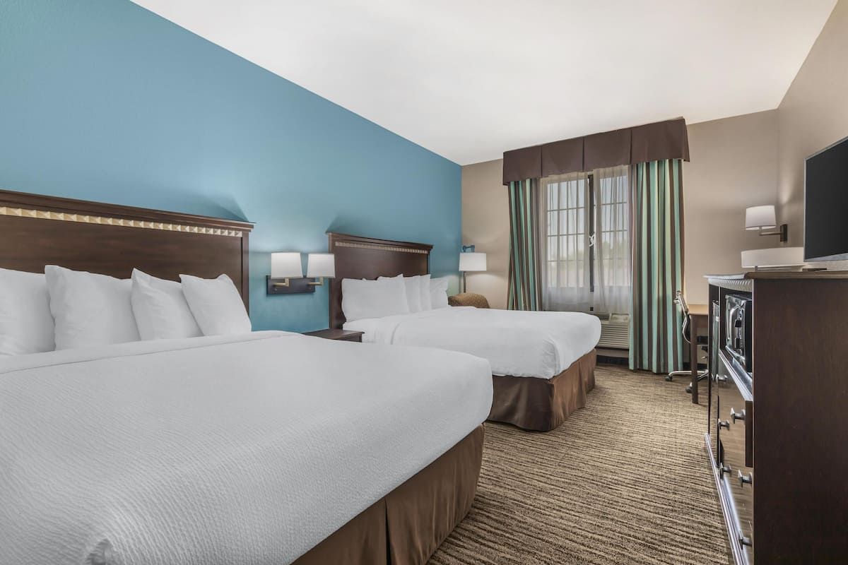 A hotel room with two beds, a TV, a desk, and a window with curtains.