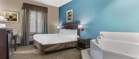 A hotel room with a bed, a desk, a chair, a dresser, a large window with curtains, a wall-mounted picture, a nightstand with a lamp, and a bathtub.