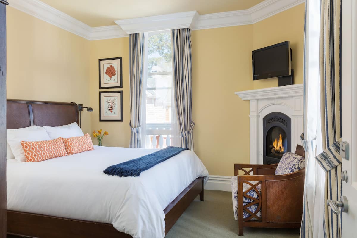 A hotel room with a large bed, a fireplace, a television, and a window with curtains.