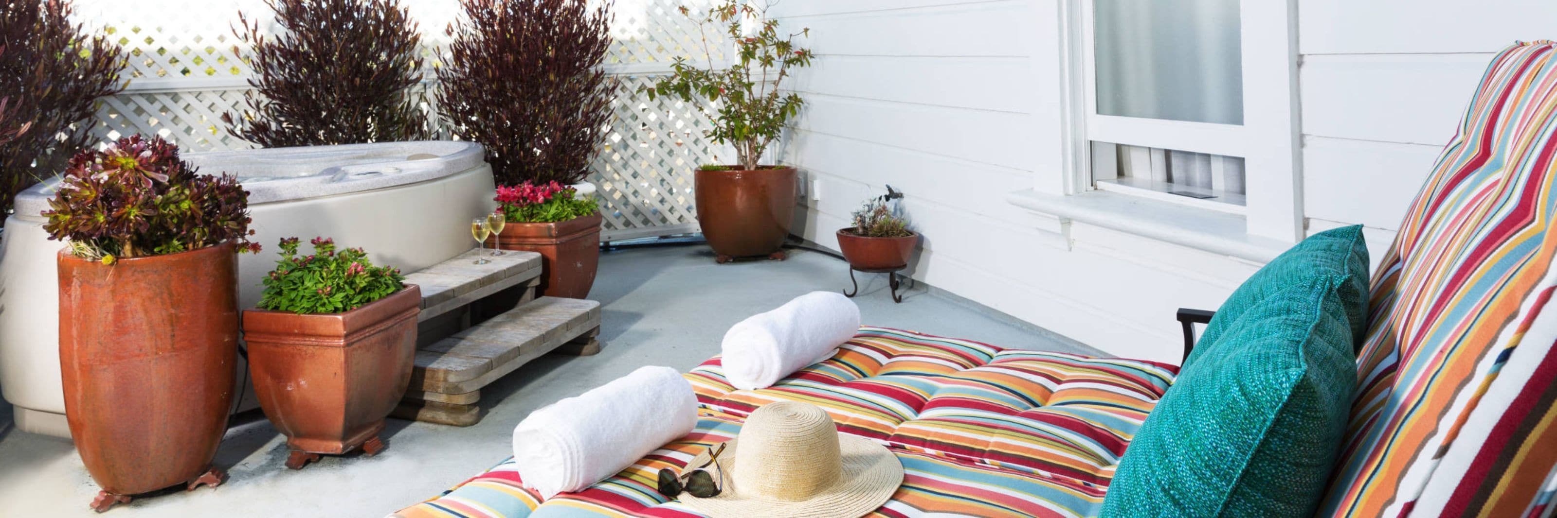 Un espacio al aire libre acogedor con un sofá, un jacuzzi y plantas en macetas.